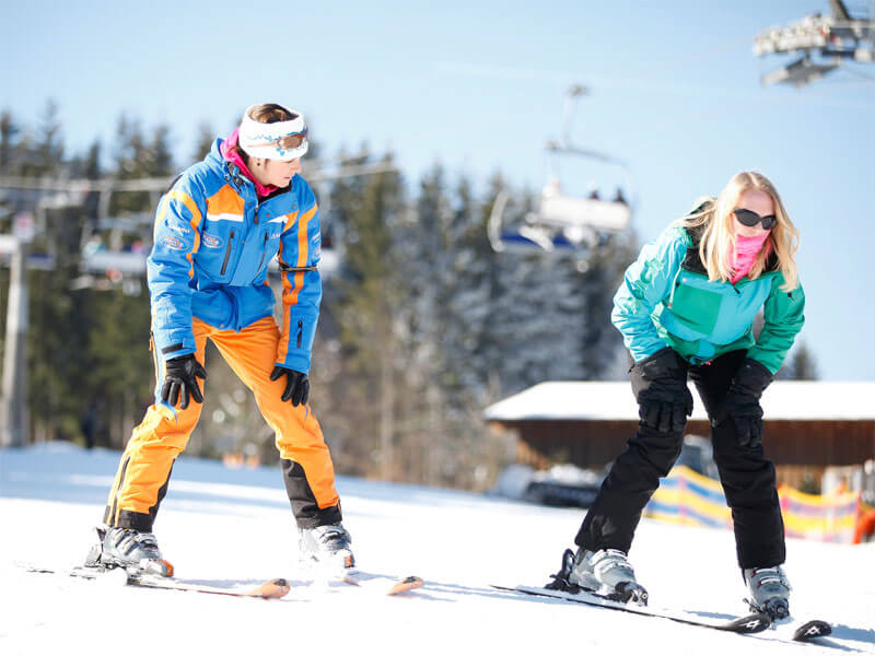 Skilehrer mit Schülerin auf Skiern auf der Piste